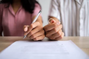 Person holding wedding ring across from another signing a document, symbolizing post-divorce estate planning.