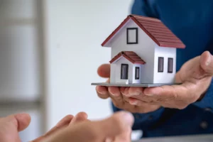 Hands offering a small red-roofed house model, symbolizing inheriting property in Ohio