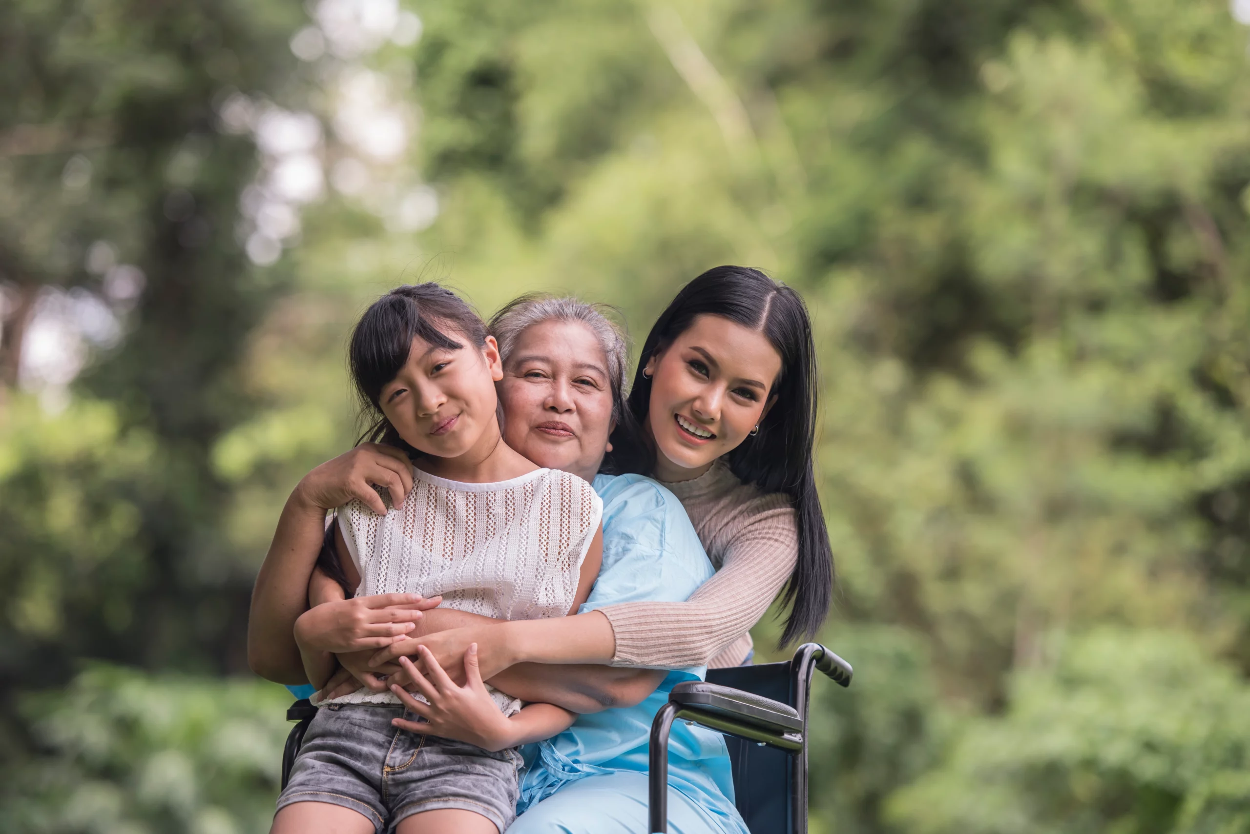 Grandmother in wheelchair embraced by daughter and granddaughter outdoors, illustrating family guardianship in Ohio.